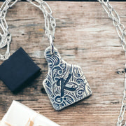 A sterling silver cow tag necklace with a floral design and an initial