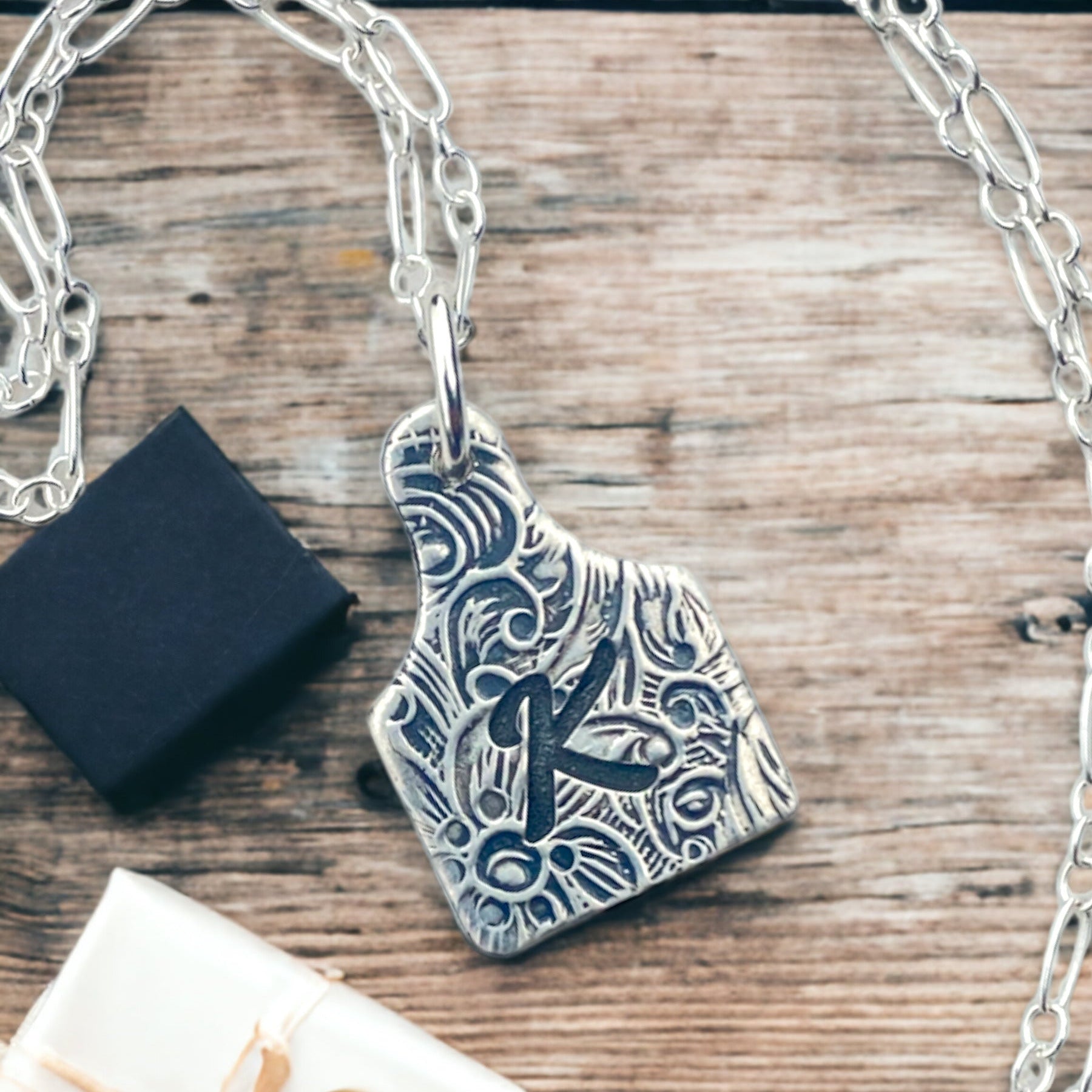 A sterling silver cow tag necklace with a floral design and an initial
